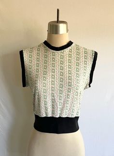 Cute 1950's repro knit crew neck tank crop top! Top is made from 1960s dainty floral poly knit with black cotton rib knit at the hem, armholes and neck.  Top is clean, but has been well loved. It is in good condition. There is some wear at the underarms and some overall fade to the colors, both in the main fabric and the rib knit trim.  Measurements: would best fit a size M Bust= 39" Bottom opening= 32" relaxed  Shoulder width= 15" Body length from side neck down to hem edge= 18" Fitted Cotton Crew Neck Vest, Retro Fitted Crew Neck Crop Top, Fitted Retro Crew Neck Crop Top, Fitted Retro Crop Top With Crew Neck, Fitted Cropped Sweater Vest For Summer, Retro Green Sleeveless Tank Top, Retro Fitted Crew Neck Tank Top, Fitted Retro Crew Neck Tank Top, Fitted Vintage Crew Neck Top