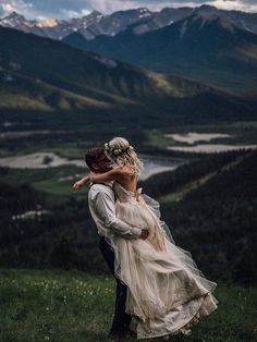 a bride and groom kissing on top of a hill with mountains in the back ground