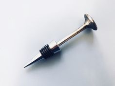 a metal object on a white surface with a screw in it's center and the tip pointing upward