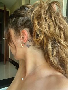 a woman with tattoos on her neck and behind her ear is looking in the mirror