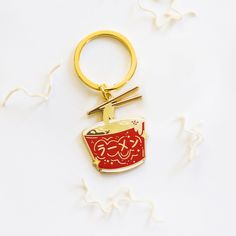 a gold keychain with a red cup and chopsticks on it