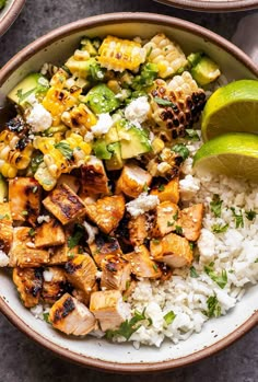 a bowl filled with rice and chicken next to two lime wedges on the side