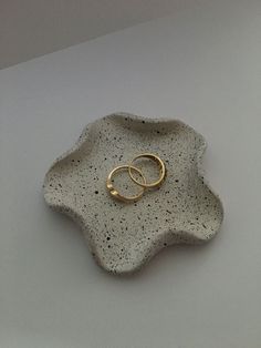 two gold wedding rings sitting on top of a white plate with black speckles