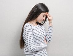 a woman holding her hand to her head while standing against a wall with the other hand on her forehead