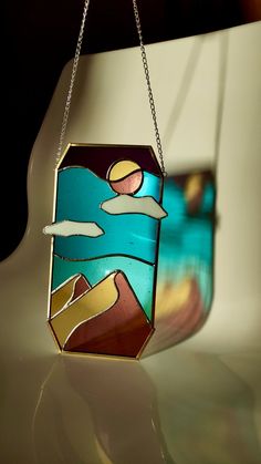 a stained glass piece hanging from a chain on a white surface with the sky and clouds reflected in it