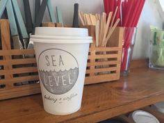 a coffee cup sitting on top of a wooden table next to cups and utensils