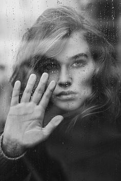 a woman holding her hand up to her face in front of a rain soaked window