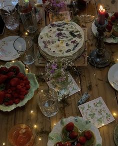 a wooden table topped with plates and bowls filled with strawberries next to lit candles