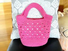 a pink crocheted purse sitting on top of a black chair next to a pillow