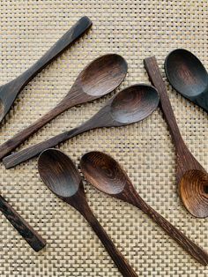 five wooden spoons are lined up on a woven tablecloth, one is black and the other is brown