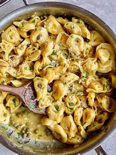 a skillet filled with pasta and sauce on top of a stove burner next to a wooden spoon