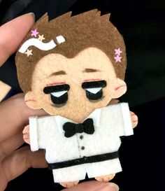 a person holding up a small doll made to look like he is wearing a tuxedo