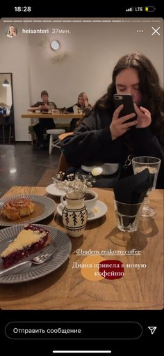 a woman sitting at a table looking at her cell phone with desserts on it