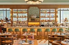 the interior of a restaurant with wooden tables, green chairs and shelves filled with liquor bottles