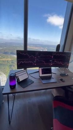 a desk with two laptops and a computer monitor on it in front of a large window