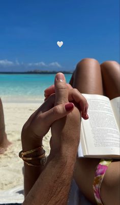 a person sitting on the beach reading a book with a white heart floating above them