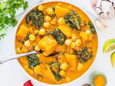 a white bowl filled with chickpea and spinach curry next to some cilantro