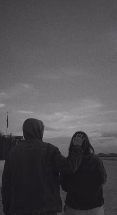 black and white photograph of two people looking out at the ocean with a kite flying in the sky