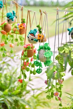 several small crocheted fruits hanging from strings in the grass with trees behind them