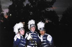 three men in blue and white marching uniforms posing for a photo with trees in the background