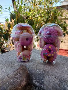 two plastic containers filled with donuts sitting on top of a rock