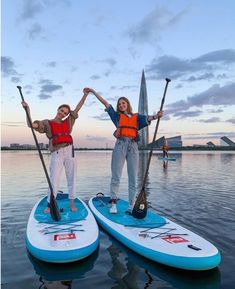 two women standing on paddle boards in the water with their hands up and holding oars