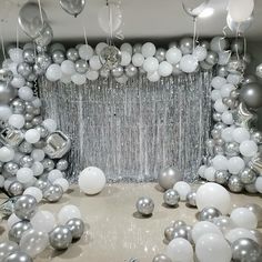 balloons and streamers are hanging from the ceiling in front of a backdrop with silver and white balls