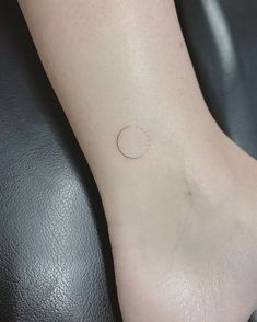 a small moon tattoo on the ankle with a tiny dot in it's center