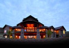 a large house lit up at night with lights on the windows and stone pillars in front