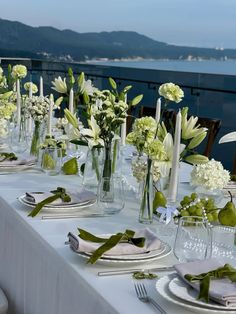 the table is set with white flowers and greenery in glass vases on each side