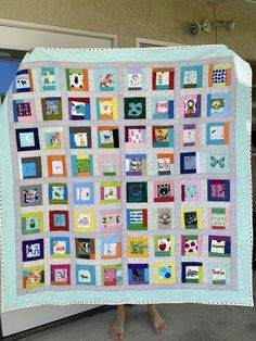 a person holding up a quilt made with squares and rectangles in different colors