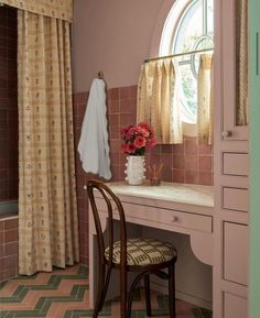 a desk with a mirror, chair and flowers on it in front of a window