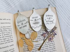 three spoons with words on them sitting next to an open book and dried flowers