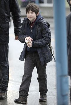 a young boy walking down the street holding an umbrella