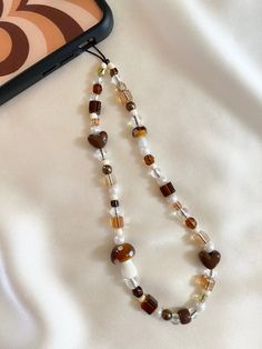 a long beaded necklace with brown and white beads is laying next to a cell phone