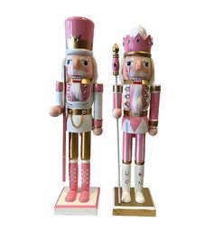 two wooden nutcrackers are standing next to each other on white background, one is pink and gold