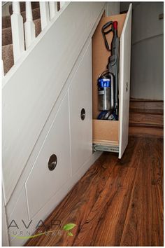 an open cabinet under the stairs with vacuum cleaner and cleaning supplies in it, on top of wood flooring