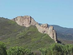 the mountains are covered with green vegetation and trees in the foreground is a clear blue sky