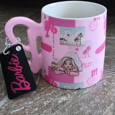 a pink coffee mug sitting on top of a counter next to a tag that says barbie