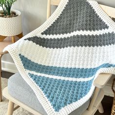 a crocheted blanket sitting on top of a chair next to a potted plant