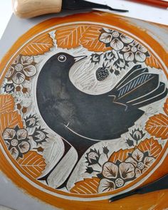 an orange plate with a black bird painted on it and two paintbrushes next to it