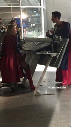 two people dressed up as superman and supergirl talking to each other in an airport