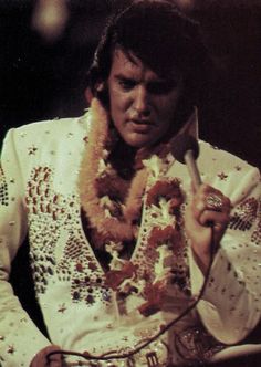 elvis presley holding a microphone in his right hand and wearing a white suit with flowers on it