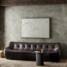 a living room with a leather couch and coffee table in front of a painting on the wall