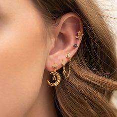 a close up of a person's ear wearing gold earrings with stars and moon designs