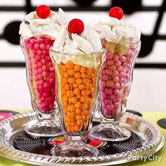 three glass vases filled with candy on top of a metal tray next to each other