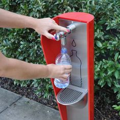 a person is filling a bottle with water from a dispenser in front of bushes