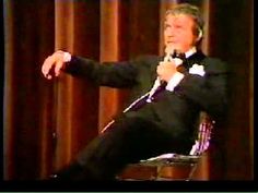 a man in a tuxedo and bow tie sitting on a chair with his hand out