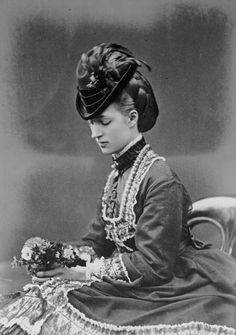 an old black and white photo of a woman in dress sitting on a chair holding flowers