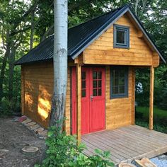 a small wooden cabin in the woods with red doors and windows on it's side